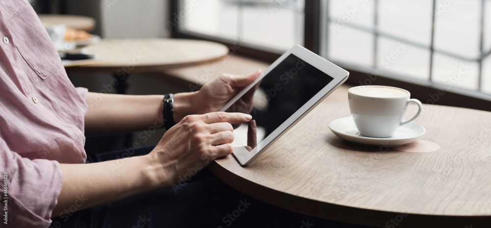 Young woman using digital tablet in cafe panoramic banner. Female hands holding digital tablet close up. Coffee break, modern lifestyle, connection, technology, business, online shopping concept Young woman using digital tablet in cafe panoramic banner. Female hands holding digital tablet close up. Coffee break, modern lifestyle, connection, technology, business, online shopping concept
