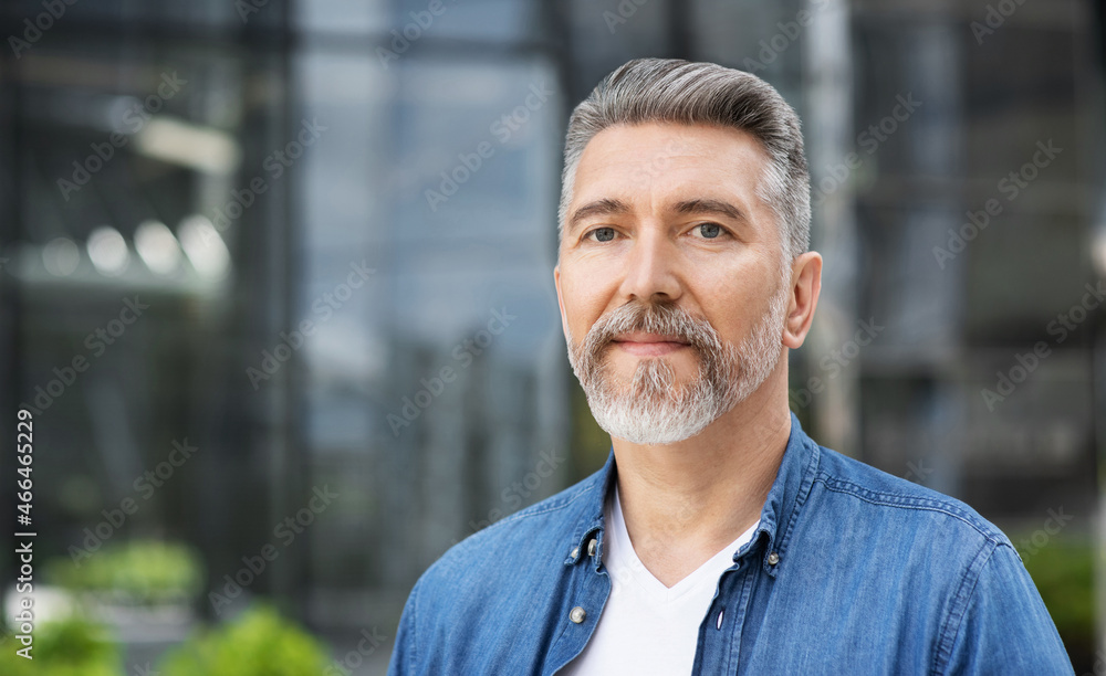Handsome smiling mature man closeup portrait. Cheerful middle age man looking at camera in a city street. Male beauty, senior lifestyle, people concept