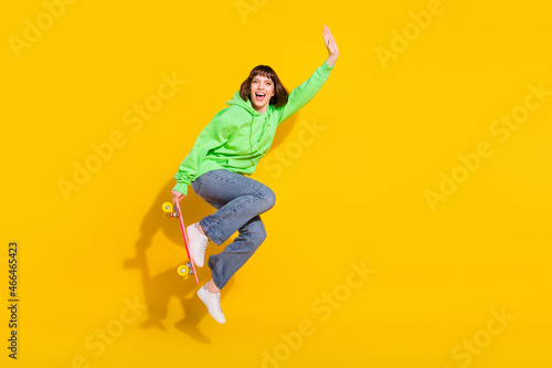 Full length body size view of attractive cheerful girl jumping riding skate pastime isolated over bright yellow color background