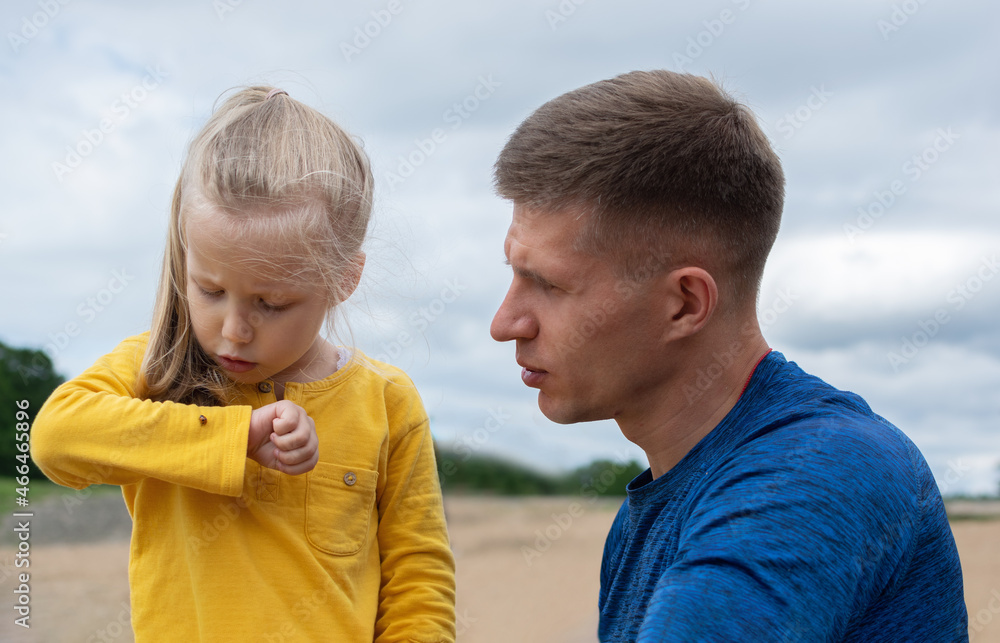 a girl and a man examine a beetle sitting on a girl's sleeve a girl and a man examine a beetle sitting on a girl's sleeve