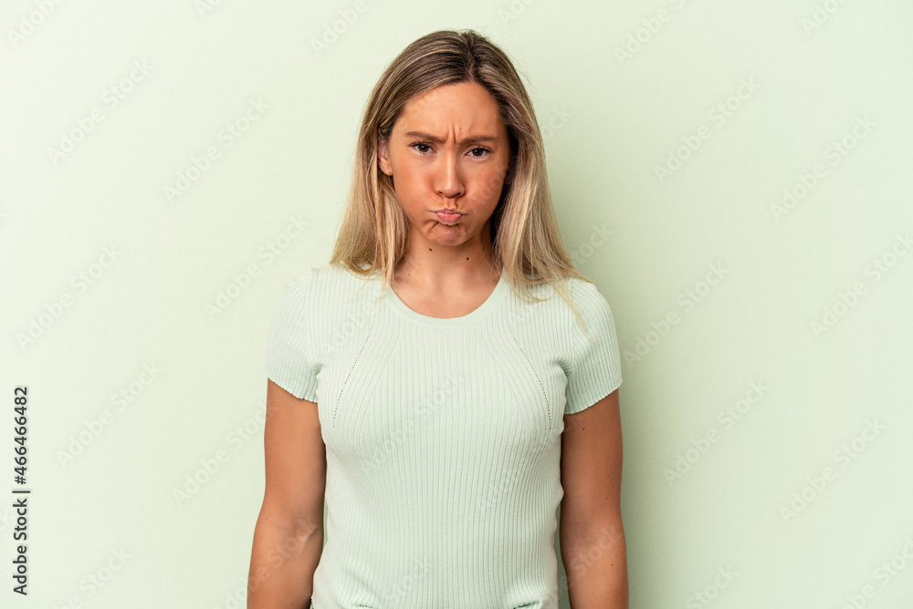 Obraz premium Young caucasian woman isolated on green background blows cheeks, has tired expression. Facial expression concept.