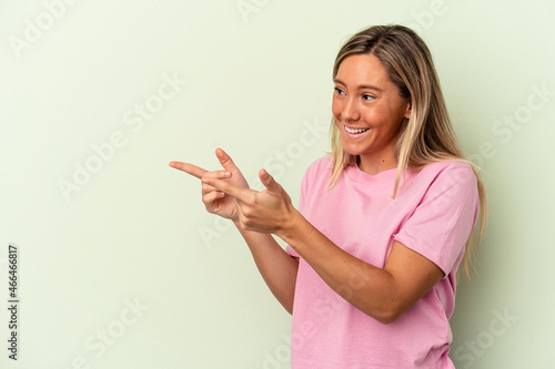 Young caucasian woman isolated on green background points with thumb finger away, laughing and carefree.