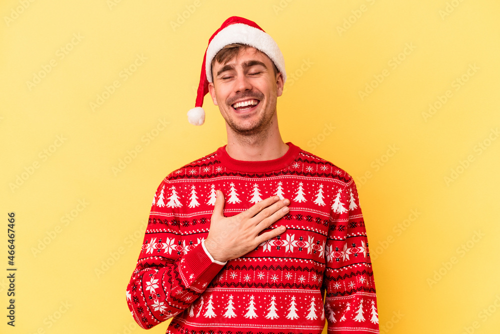 Young caucasian man celebrating Christmas isolated on yellow background laughs out loudly keeping hand on chest. Young caucasian man celebrating Christmas isolated on yellow background laughs out loudly keeping hand on chest.