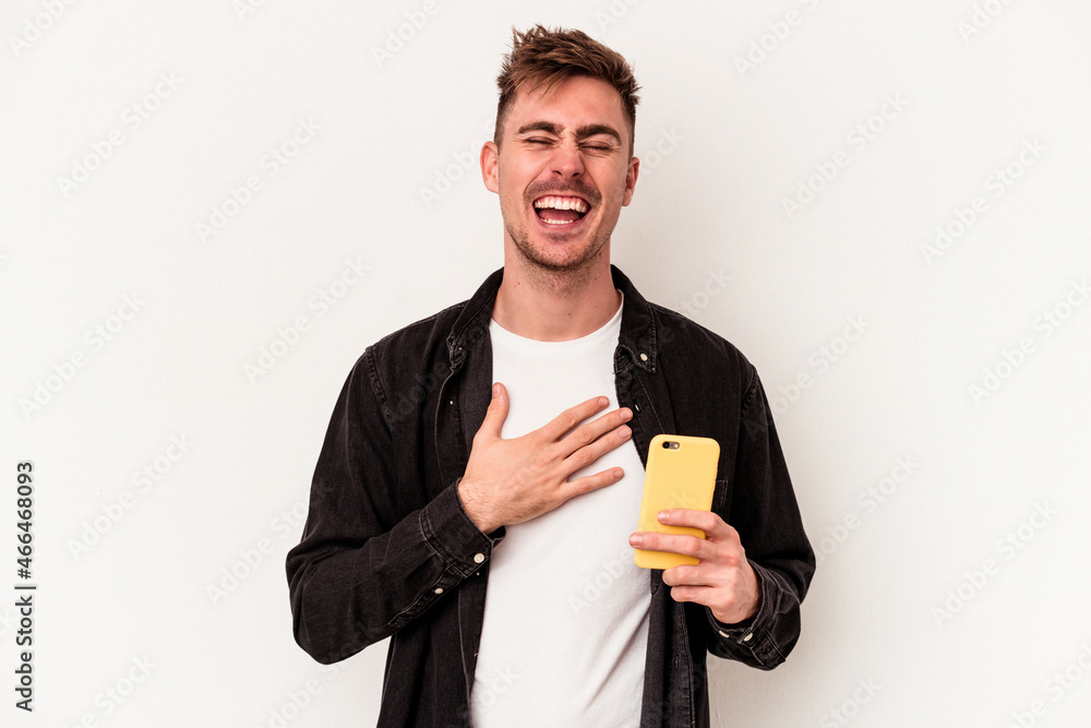 Young caucasian man holding a mobile phone isolated on white background laughs out loudly keeping hand on chest. Young caucasian man holding a mobile phone isolated on white background laughs out loudly keeping hand on chest.