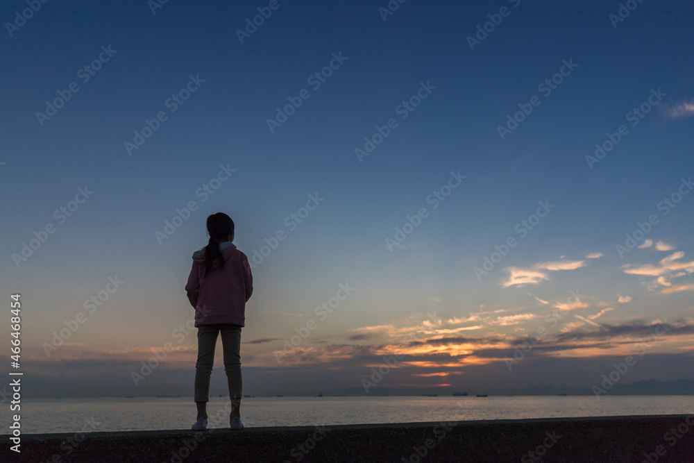 夕方の海岸で空の夕焼けを見ている小学生の子供の姿