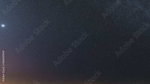 Night Starry Sky With Glowing Stars Above Countryside Field Landscape In Early Spring. Bright Glow Of Planet Venus In Sky Among The Milky Way Galaxy Stars. Sky In Lights Of Sunset Dawn. 4K Timelapse