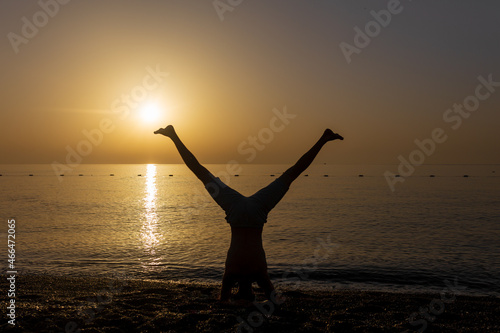 a man's silhouette, which doing yoga balance on the sunset beach