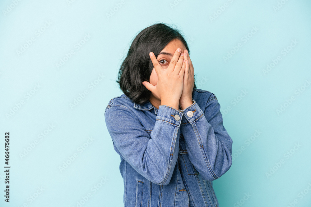 Young latin woman isolated on blue background blink through fingers frightened and nervous. Young latin woman isolated on blue background blink through fingers frightened and nervous.