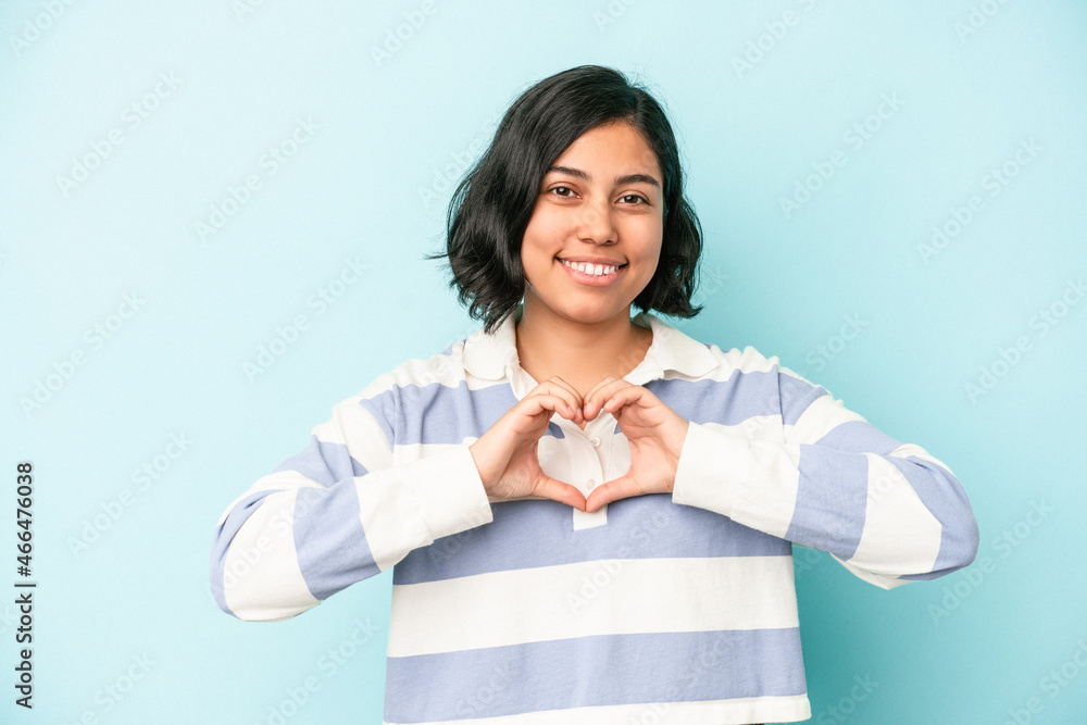 Young latin woman isolated on blue background smiling and showing a heart shape with hands. Young latin woman isolated on blue background smiling and showing a heart shape with hands.