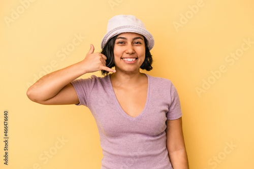 Young latin woman isolated on yellow background showing a mobile phone call gesture with fingers.