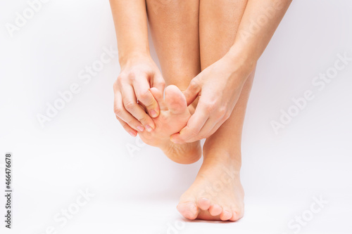 Pain in the foot and toes from uncomfortable shoes. A woman holds a sore foot with her hands on a white background. Pathology of bone structures, flat feet. Cramp, convulsion, spasm. Orthodontics © Марина Демешко