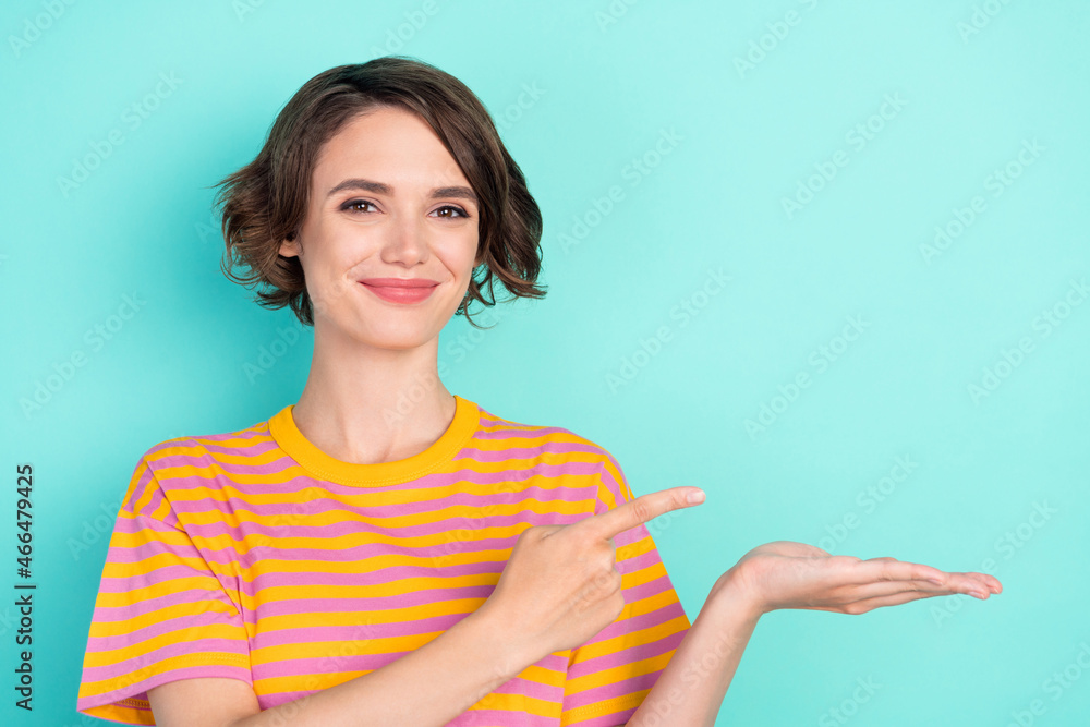 Photo of adorable cute young woman dressed striped t-shirt smiling holding arm pointing empty space isolated teal color background Photo of adorable cute young woman dressed striped t-shirt smiling holding arm pointing empty space isolated teal color background