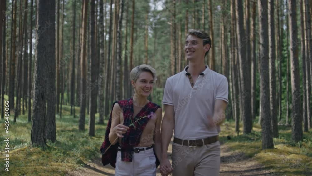 Young couple, woman and man walk hand in hand, talk happily. Cute millennials on stroll in forest or national park. Authentic smiles and real feelings. Portrait of young couple Young couple, woman and man walk hand in hand, talk happily. Cute millennials on stroll in forest or national park. Authentic smiles and real feelings. Portrait of young couple