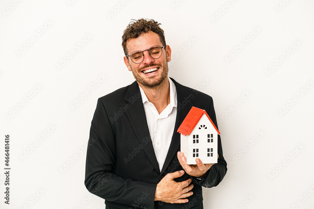 Young caucasian real estate holding a toy home isolated on white background laughing and having fun. Young caucasian real estate holding a toy home isolated on white background laughing and having fun.