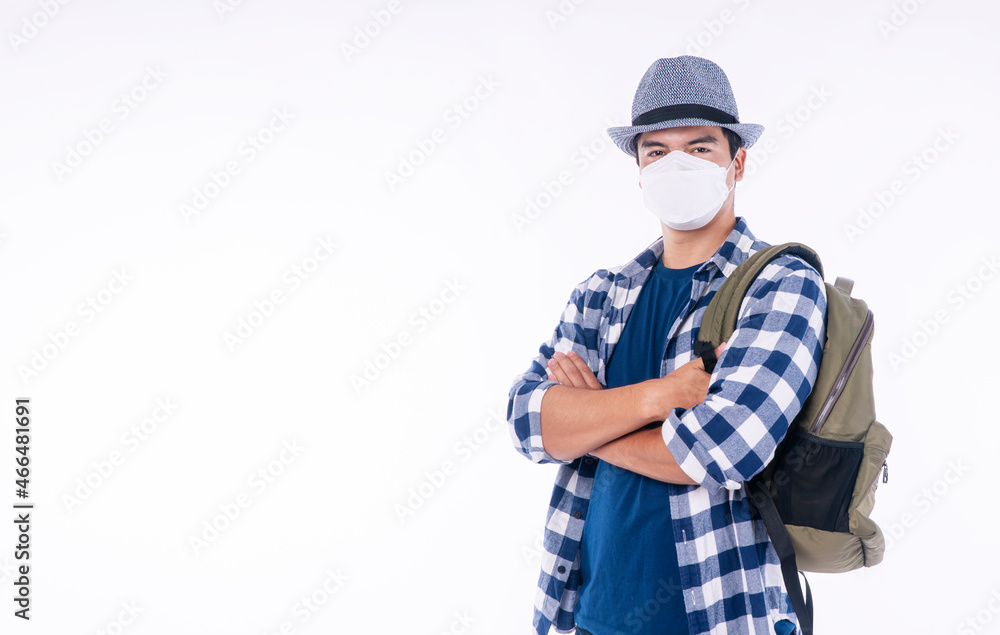 New normal lifestyle travel vacation concept. Traveler adventure handsome young man wear casual shirt, hat and protective mask safety with backpack while standing over isolated background New normal lifestyle travel vacation concept. Traveler adventure handsome young man wear casual shirt, hat and protective mask safety with backpack while standing over isolated background