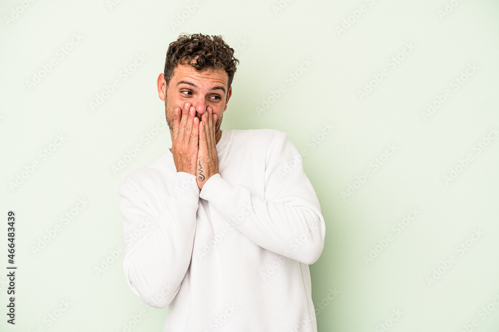 Young caucasian man isolated on green background laughing about something, covering mouth with hands. Young caucasian man isolated on green background laughing about something, covering mouth with hands.