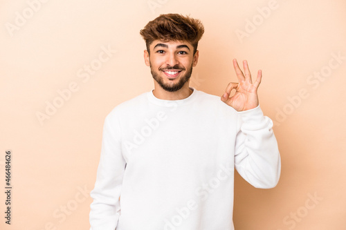 Young arab man isolated on beige background cheerful and confident showing ok gesture.