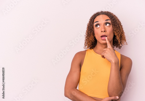 Young latin transsexual woman isolated on pink background looking sideways with doubtful and skeptical expression.