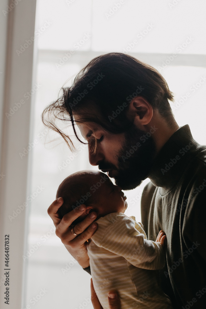 Silhouette Of A Stylish Bearded Father Kisses A Sleeping Newborn Girl