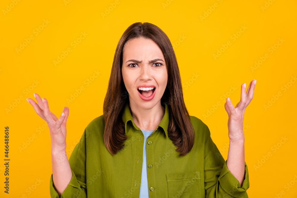 Photo of angry upset young lady wear green shirt rising arms shouting isolated yellow color background
