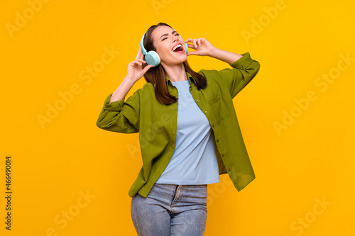 Photo of sweet adorable young lady wear green shirt earphones smiling singing dancing isolated yellow color background