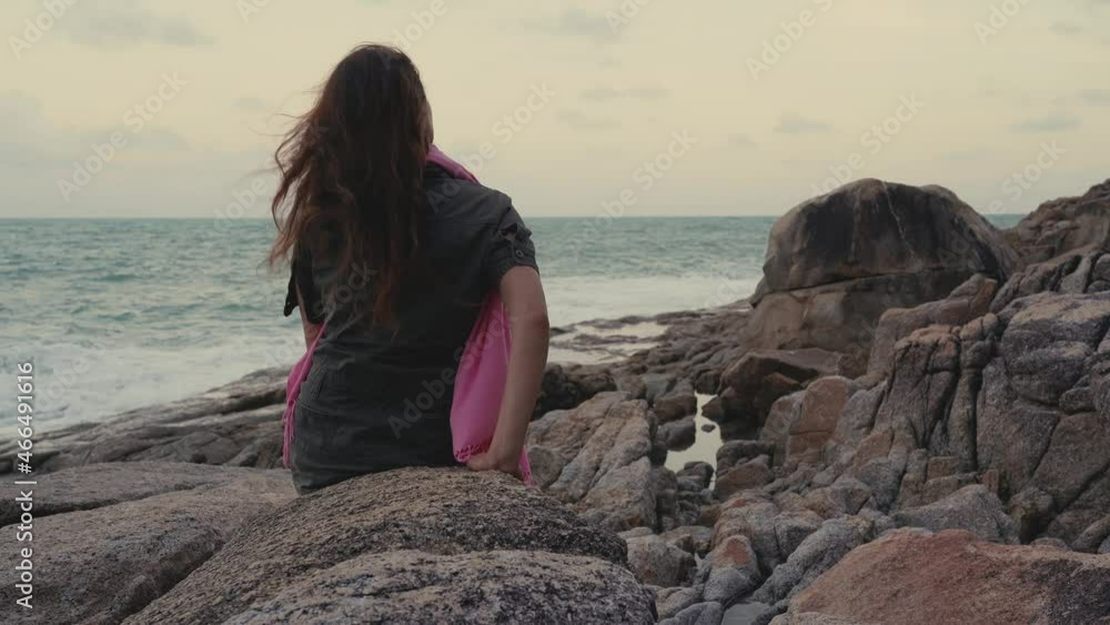 Young sad woman with long hair sitting alone on rocks by the sea Young sad woman with long hair sitting alone on rocks by the sea