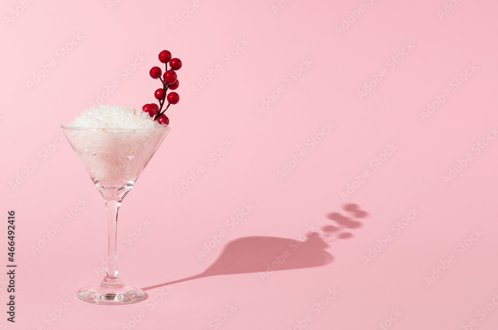 Cocktail glass with snow and holly berries against pink background. Creative Christmas concept.