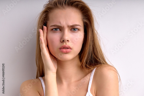 Upset female touching face  having dissatisfied facial expression  looking at camera  isolated on white studio background. Portrait of attractive lady with natural hair and beauty is misunderstanding