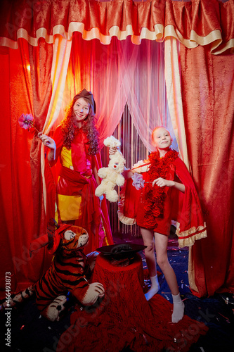 Family during a stylized theatrical circus photo shoot in a beautiful red location. Models mother and daughter posing on stage with curtain