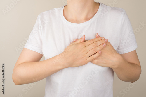 Cropped closeup photo of woman in white t-shirt holding her hands on heart on isolated grey background