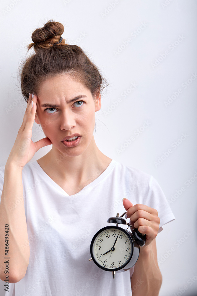 young lady with alarm clock awakening hard early wearing casual white t-shirt posing isolated on white studio background. caucasian woman has no enough sleep, want more rest at weekends. copy space young lady with alarm clock awakening hard early wearing casual white t-shirt posing isolated on white studio background. caucasian woman has no enough sleep, want more rest at weekends. copy space