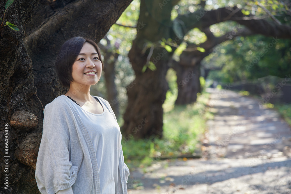 早朝の新緑の中でほほ笑む40代日本人女性