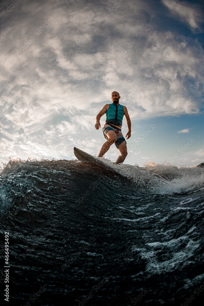 man wakesurfer actively balancing on wakeboard along the river wave