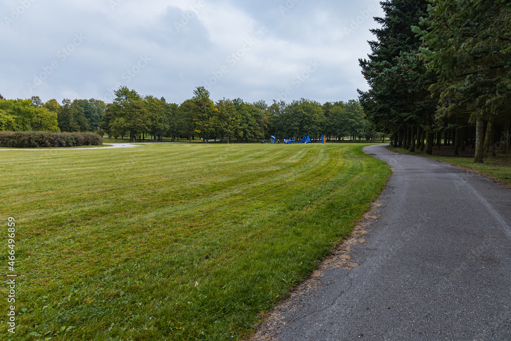 Long asphalt path in Citadel park with trees and lamps around next to big green glade