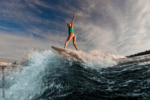 young attractive woman with raised arms balances on splashing wave on wakesurf