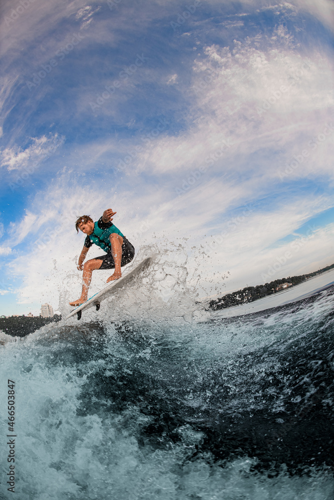 Active man wakesurfer dressed in vest jumping up over splashing wave against cloudy sky Active man wakesurfer dressed in vest jumping up over splashing wave against cloudy sky