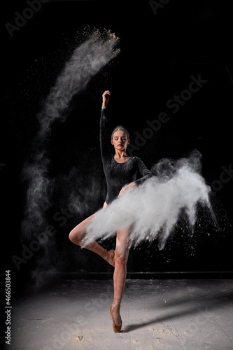 Dramatic portrait of strong and talented female dancer with white powder explosion  moving in dust  flour. Graceful gorgeous woman in black bodysuit in slow motion