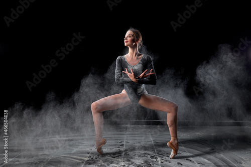 Flexible woman dancing with flour on black background in studio  moving with legs apart. Talented athlete ballet dancer in bodysuit in slow motion  looking at side  making dance tricks.