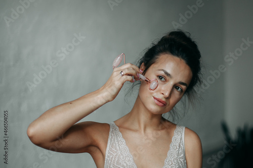 A brunette woman 30 years old with a bundle on her head in underwear at home in the bathroom does a face massage with a gouache scraper