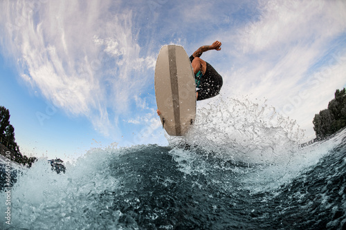 beautiful view of a wakesurf board and man jumping in the air above a splashing wave