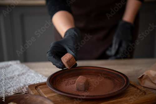 Hands in black gloves keep chocolate candy. Brown dish with truffles. Copy space. Close-up.
