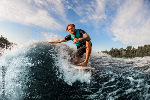 athletic guy wakesurfer skilfully riding down the blue splashing wave on a warm day