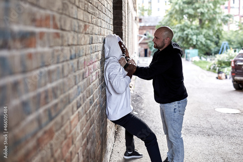 Street theif commits robbery attack on african man, at day time. Young frightened black afro man is being assaulted by dangerous angry man in alley. Crime and Aggression concept. Side view photo