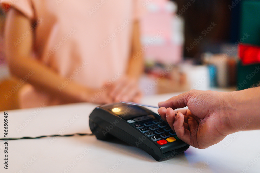 Close-up view of unrecognizable male customer paying with NFC technology by credit card contactless on POS terminal, selective focus, blurred background. Contactless payment using debit card.