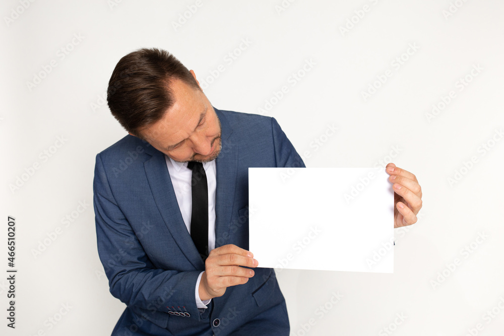 Attractive man, businessman in business suit and tie bent over blank white sheet of paper for inscription. Copy space, studio shot, white background. Attractive man, businessman in business suit and tie bent over blank white sheet of paper for inscription. Copy space, studio shot, white background.