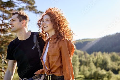 Side view portrait of smiling happy redhead woman and man hikers travelling together, looking at side, inc asual wear, curly woman enjoying nature around, in forest. people lifestyle concept