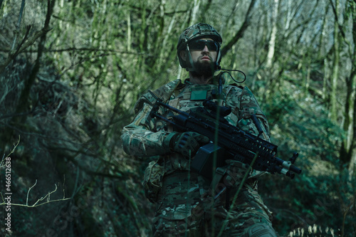 Portrait of airsoft player in professional equipment with machine gun in the forest. Soldier with weapons at war