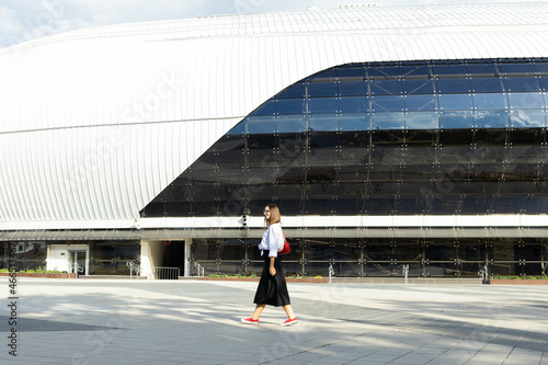 A young woman in a white shirt and black skirt is walking around the city