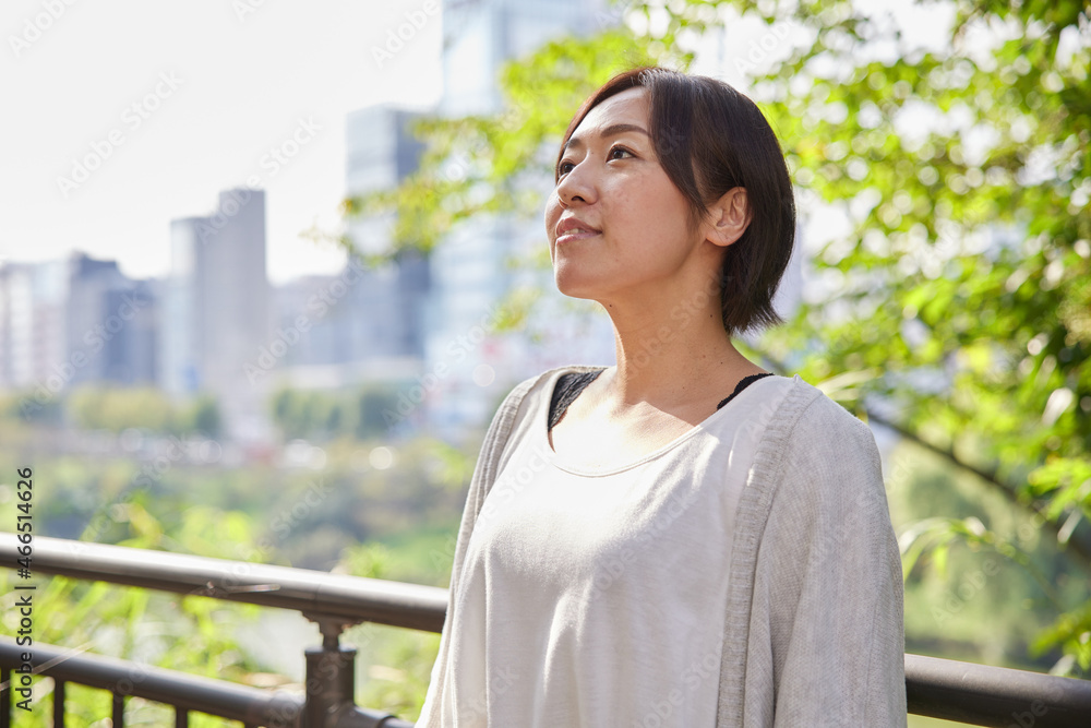 早朝の新緑の中でほほ笑む40代日本人女性