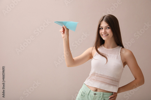 Beautiful teenage girl with paper plane on beige background. Space for text